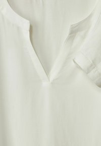 Blusa bianca con scollo a V, maniche corte arrotolate e texture del tessuto liscia. Design semplice con pochi dettagli di cucitura.