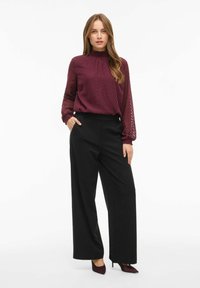 Blusa burdeos de cuello alto con un patrón de espiga; combinada con pantalones de pierna ancha negros de cintura alta y tacones puntiagudos burdeos.