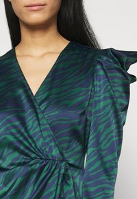 Long-sleeve dress in teal and navy satin with a wrap design, featuring a tiger stripe pattern and gathered detail at the waist.