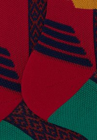 Calzini multicolori con una texture lavorata a maglia. Presentano strisce rosse, verdi e marine, modelli geometrici e sezioni del piede e del tallone a contrasto.