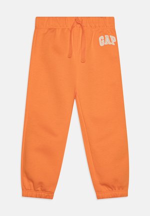 Pantalon de survêtement orange avec une taille élastique, un cordon de serrage, des chevilles côtelées et un logo "GAP" blanc sur la cuisse gauche. Texture douce.