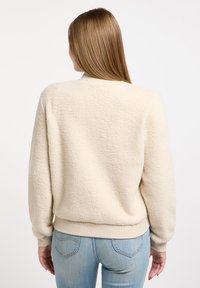 Cream fleece sweatshirt with a relaxed fit, ribbed cuffs, and waistband. Features a soft texture and appears slightly oversized.