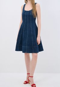Tumman denim-mekko, jossa on istuva bodice ja levenevä hame, ja siinä on pystysaumat. Yhdistetty punaisiin korkokenkiin.