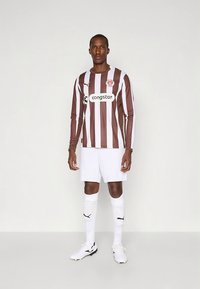 Nogometni dres z dolgimi rokavi z rjavimi in belimi črtami, bele kratke hlače in nogavice. Na sprednji strani so logotip Puma in tekst sponzorja. Vključno s črnimi kopačkami.