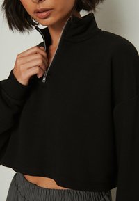 Schwarzer, verkürzter Sweatshirt mit hohem Kragen und halbem Reißverschluss, aus weichem Stoff gefertigt. Verfügt über weite Ärmel und eine glatte Textur.