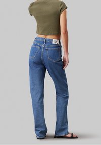 Tmavě modré džíny s vysokým pasem a rovnými nohavicemi, s kapsami vzadu a aplikací loga CK na pase. Texturovaný denimový materiál.