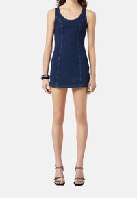 Mörkblå denim miniklänning med en åtsittande form, rund halsringning och synliga sömmar. Buren med svarta klackskor med remmar och ett kraftigt armband.