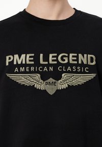 Felpa nera con un logo ricamato in beige ben visibile: "PME LEGEND" sopra "AMERICAN CLASSIC" con elementi di design a forma di ali e scudo.