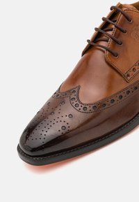 Scarpe eleganti in pelle marrone dal design raffinato, punta appuntita, perforazioni decorative e accenti scuri a contrasto sulla tomaia.