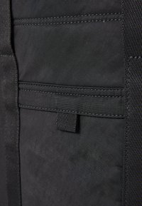 Borsa in tessuto nero con diversi scomparti, un motivo testurizzato e una robusta tracolla intrecciata. Cuciture rinforzate lungo le giunture.