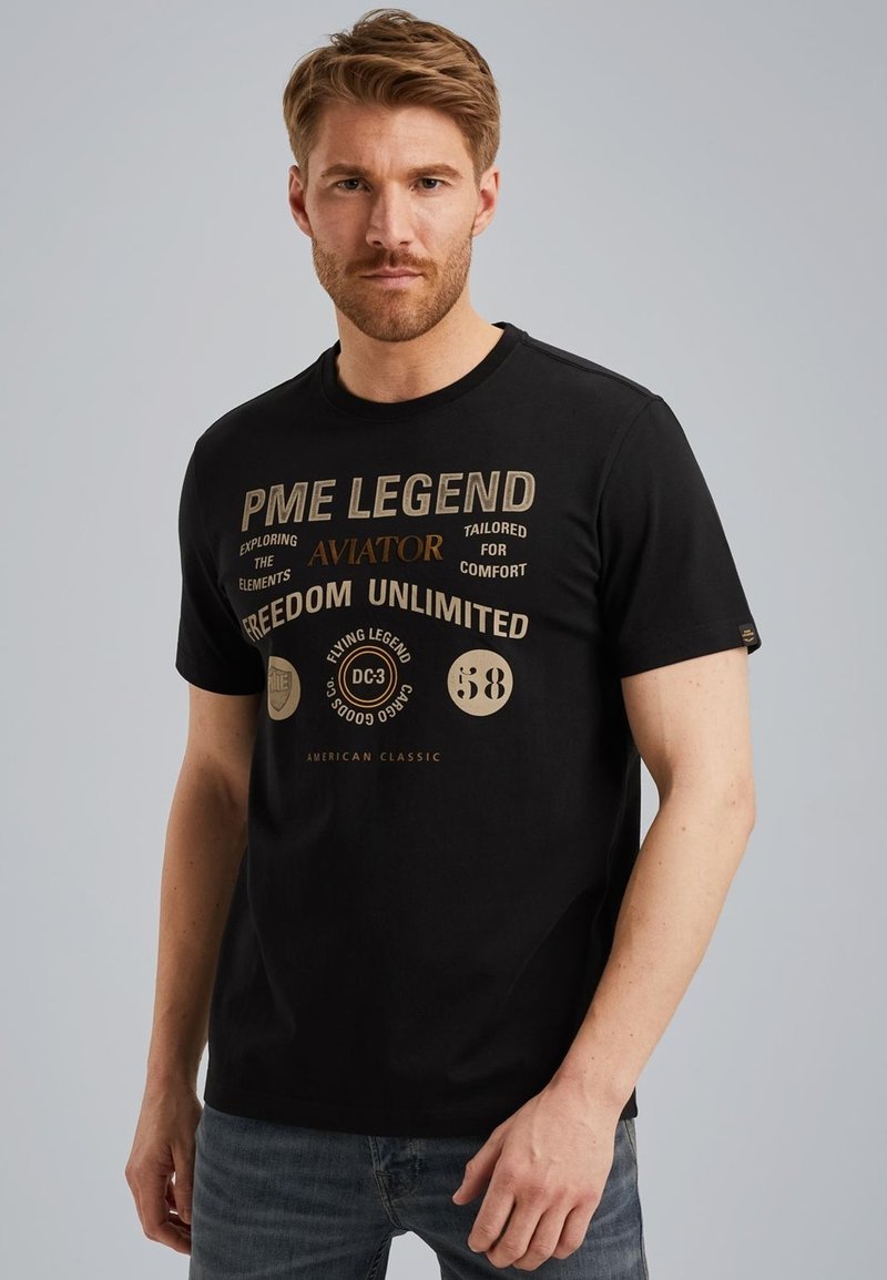 Camiseta de algodón negra con texto y logotipos impresos en dorado, mangas cortas y cuello redondo. Diseño sencillo sin patrones adicionales.