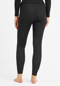 Person barefoot wearing fitted black ribbed leggings and a matching long-sleeve top, standing against a plain white background.