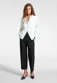 Camicia bianca con colletto, abbinata a pantaloni neri a gamba larga con risvolti e décolleté neri a punta.