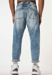 Jeans de denim azul claro con corte holgado, que cuentan con cinco bolsillos, un desvanecimiento sutil y puños enrollados. Cintura elástica con detalle de logo.