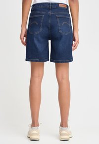 Tamsiai skalbti džinsiniai šortai, prigludę modelio, su matomomis siūlėmis. Turi du galinius kišenes su lenkta siuvimo detale, derinami su šviesiais sportbačiais.