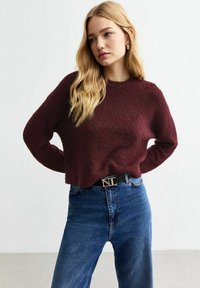 Burgundy texturerad tröja med rund halsringning, kombinerad med högmidjade blå jeans och ett svart bälte med en detalj i guld.