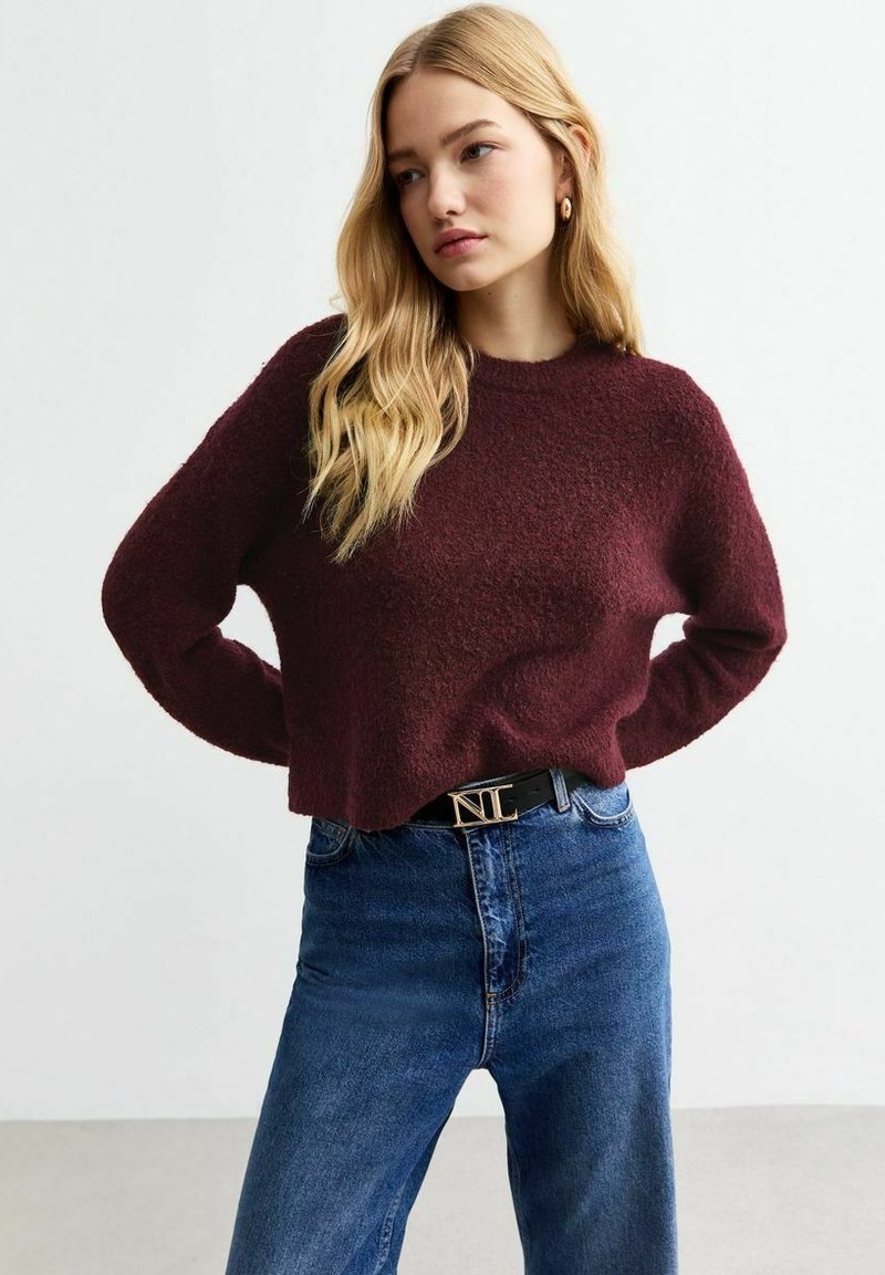 Burgundy texturerad tröja med rund halsringning, kombinerad med högmidjade blå jeans och ett svart bälte med en detalj i guld.