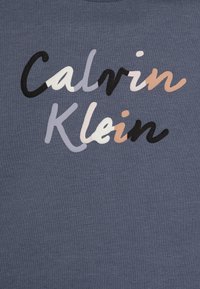 Niebieska bawełniana koszulka z napisem "Calvin Klein" w różnych kolorach: czarnym, jasnoszarym, białym i beżowym, o miękkiej teksturze i luźnym kroju.