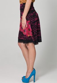 Gonna a motivo floreale nera con accenti rosa, con dettagli scritti. Mostra un design svasato e un orlo a strati. Tacchi alti blu.