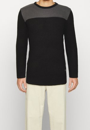 Gestrickter Pullover mit einem schwarzen Körper und einem grauen oberen Bereich, geripptem Muster, rundem Halsausschnitt und langen Ärmeln. Schlichte Gestaltung mit dezentem Branding.