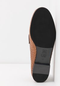 Brown leather shoe with a textured crocodile pattern, black rubber sole, and a smooth heel. Features embossed brand and material details.