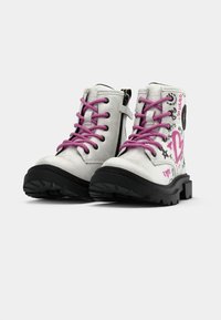 Stivaletti bianchi alla caviglia con suole nere, lacci rosa, cerniera laterale e design di cuori rosa in stile graffiti con testo nero.