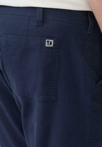 Marineblauwe broek van gestructureerde stof, met een achterzak en een klein logo-opdruk in vierkante vorm.
