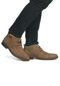 Bottines en daim marron avec bouts ronds, lacées à l'avant, avec des détails de couture et un petit talon en caoutchouc, portées avec un jean foncé.