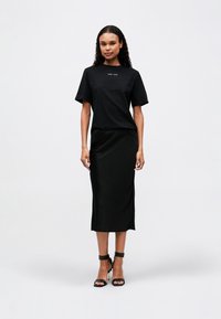 Black cotton t-shirt with short sleeves, paired with a black, knee-length satin skirt. Worn with black strappy heels.