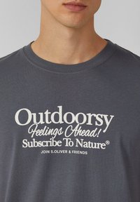 Grijze katoenen t-shirt met een ronde hals, korte mouwen en opvallende witte tekst: "Buitenlevensgevoelens Vooruit! Abonneer je op de Natuur."