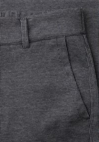 Close-up of grey fabric with small black and white check pattern showing waistband, belt loop, and front pocket seam of trousers.