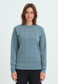 Hellblaues Sweatshirt mit geometrischem Muster in dunklen Farbtönen, gerippten Bündchen und Saum. Weicher Stoff, Rundhalsausschnitt.