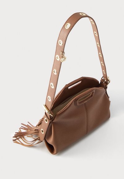 Καφέ δερμάτινη τσάντα ώμου με φαρδιά λουρίδα που διαθέτει χρυσά τρουκς και λεπτομέρεια με φουντίτσα, ανοιχτό πάνω μέρος που αποκαλύπτει απαλό εσωτερικό επένδυμα.