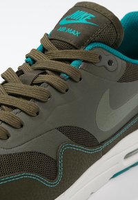Nike Air Max Sneaker in Olivgrün mit Mesh- und synthetischen Materialien, türkisfarbenen Akzenten, strukturierten Details und weißer Sohle.