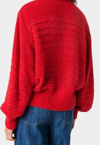 Czerwony sweter z dzianiny o teksturowanym wzorze, szerokimi rękawami i ściągaczem u dołu. Tył prezentuje poziomy wzór ściągacza.