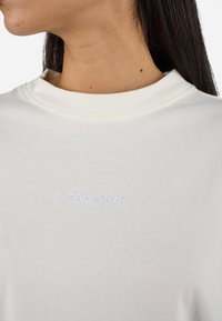Cream-colored t-shirt with a relaxed fit, featuring a ribbed crew neckline and embroidered "PECADOR" logo in white on the chest.