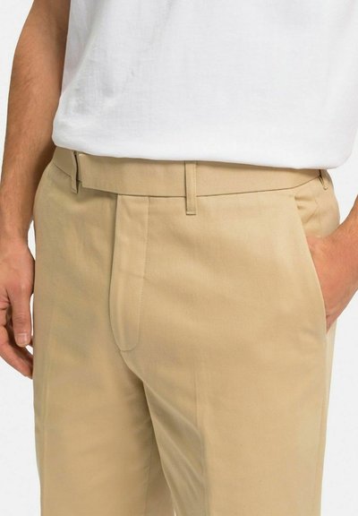 Beige bomullbyxor med flat fram, sidofickor och bälteshällor. Tyget har en mjuk struktur och en skräddarsydd passform.