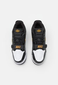 Czarno-białe trampki z skórzanym cholewką, perforowanym miejscem na palce, złotymi akcentami i paskiem z logo "NIKE" na śródstopiu.