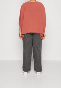 Locker sitzendes, rostfarbenes Oberteil mit kurzen Ärmeln; kombiniert mit grauen, weit geschnittenen Hosen. Glatter Stoff mit einer weichen, strukturierten Oberfläche.