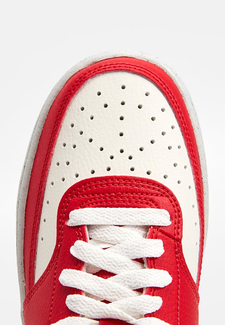 Chaussure de sport rouge et blanche en cuir avec un bout perforé, de grosses lacets blancs, et un contraste de couture sur le dessus.