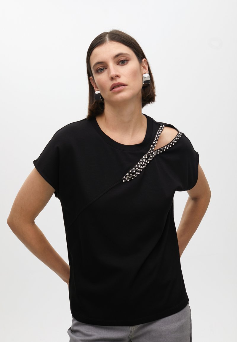 Black short-sleeve top with asymmetrical neckline, featuring a decorative band of clear gemstones across the shoulder. Smooth texture.