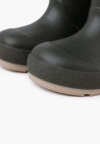 Bottes en caoutchouc vert foncé avec une semelle texturée crème. Le design présente un bout rond et un dessus lisse avec des coutures discrètes.