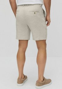 Vaaleat pellavashortsit, joissa on takataskut ja kultanapit, tarjoavat hyvin istuvan leikkauksen ja sileän pinnan. Yhdistettynä vaaleanruskeisiin lenkkareihin.