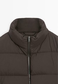 Giacca a vento marrone scuro con colletto alto, chiusura con zip e texture trapuntata con imbottitura orizzontale.