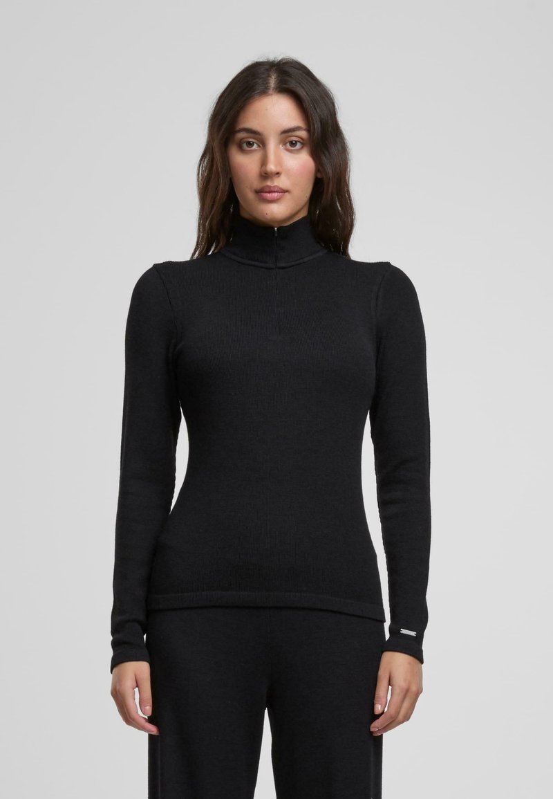 Maglietta nera a maniche lunghe con colletto alto e chiusura a mezza zip. Realizzata in un materiale a costine, presenta un design aderente e dettagli delle cuciture sottili.