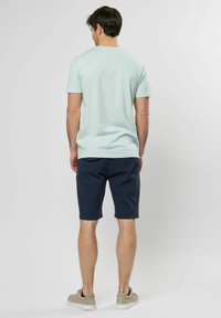 Miętowa koszulka z krótkim rękawem, granatowe szorty i beżowe trampki. Casualowy fason z okrągłym dekoltem i gładką, jednolitą tkaniną.