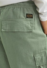 Shorts cargo vert kaki avec une taille élastique, dotés d'une poche à patch et d'un tissu texturé. Comprend une étiquette de marque.