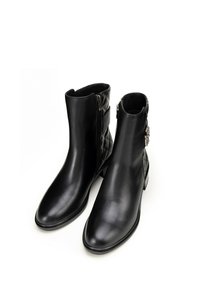 Botas de tobillo de cuero negro con un acabado suave, que presentan un tejido acolchado en la parte posterior, cremalleras laterales y acentos decorativos de metal.