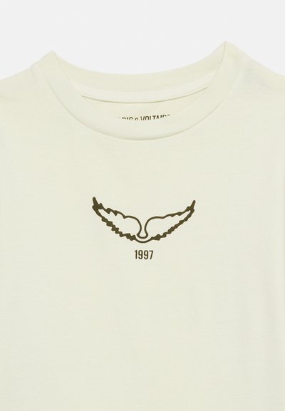 Camiseta de cuello redondo color blanco roto con gráfico de ala negra y "1997" impreso justo debajo, centrado en el pecho.