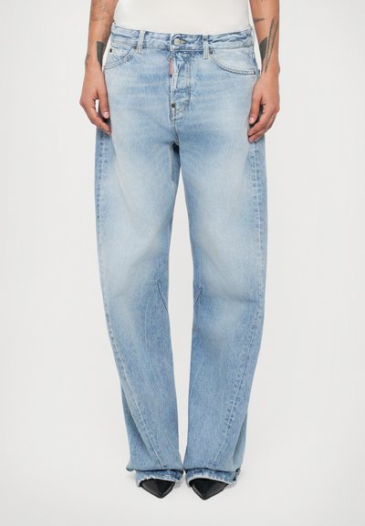 Hellblaue Jeans aus Denim mit lockerer Passform, ausgestattet mit einem Knopfverschluss, fünf Taschen und leichtem Ausbleichen. Am Ende ausgestellte Beine über schwarzen spitzen Absätzen.